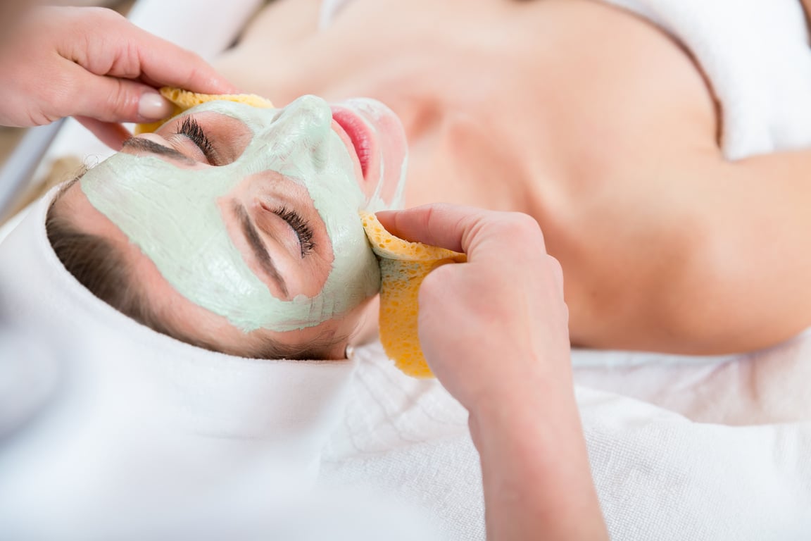 Female Cosmetologist Cleansing Client Face with Sponge